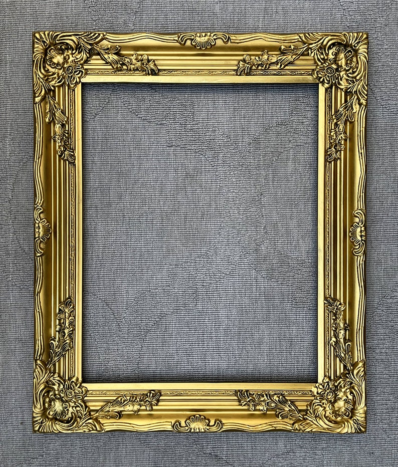 May include: A gold ornate picture frame with intricate carvings and a raised edge. The frame is against a gray textured background.