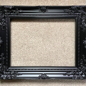 Pode incluir: Uma moldura de imagem preta adornada com um design decorativo e detalhado. A moldura é feita de madeira e tem um acabamento liso e brilhante.