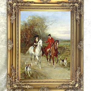 Puede incluir: Una pintura al &oacute;leo en un marco dorado decorativo que representa a dos jinetes a caballo, uno en un caballo blanco y otro en uno marr&oacute;n, acompa&ntilde;ados por dos peque&ntilde;os perros de caza en un camino de tierra rodeado de &aacute;rboles y campo.