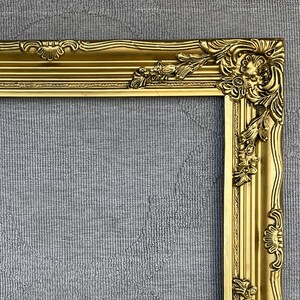 May include: A gold ornate picture frame with a decorative, intricate design. The frame is made of wood and has a glossy finish.
