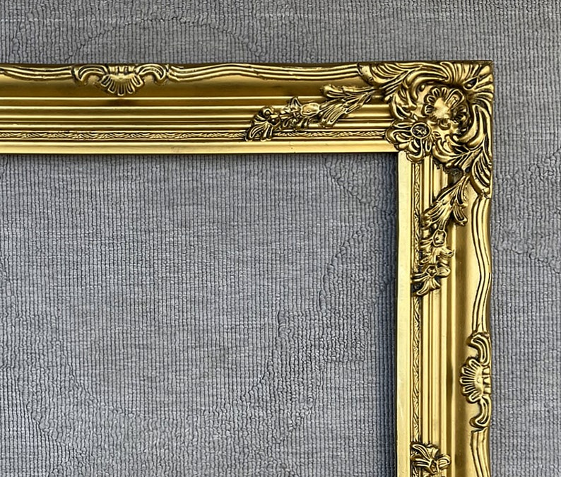 May include: A gold ornate picture frame with a decorative, intricate design. The frame is made of wood and has a glossy finish.