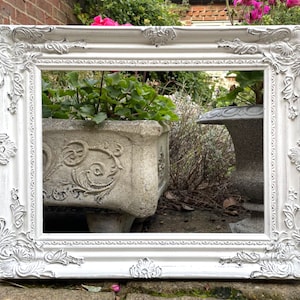 May include: White ornate picture frame with a distressed finish. The frame is made of wood and has a raised design around the edges.