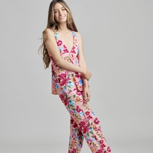 May include: A light pink pajama set with a floral pattern. The set includes a sleeveless top and matching pants. The floral design features red, pink, blue, and yellow flowers. The pajama set is made of a soft, lightweight fabric.