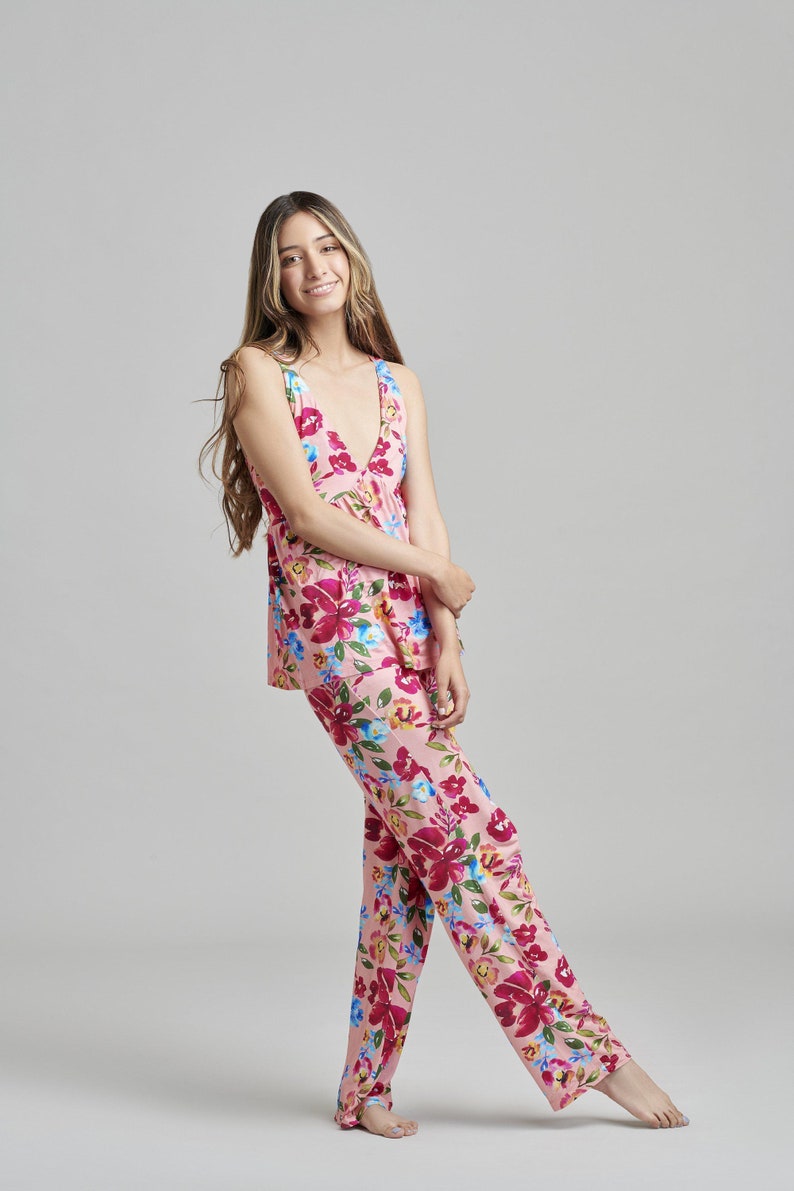 May include: A light pink pajama set with a floral pattern. The set includes a sleeveless top and matching pants. The floral design features red, pink, blue, and yellow flowers. The pajama set is made of a soft, lightweight fabric.