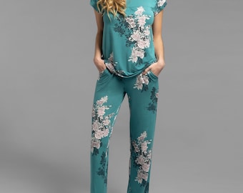 May include: Teal-colored pajama set with a floral pattern. The set includes a short-sleeved top and matching pants. The floral design features white and gray flowers. The model is wearing the pajama set.