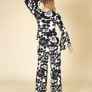 May include: A two-piece outfit featuring a black and white floral pattern. The top has long, flared sleeves and a wrap-style design. The matching pants are wide-legged. The outfit is made of a lightweight fabric.