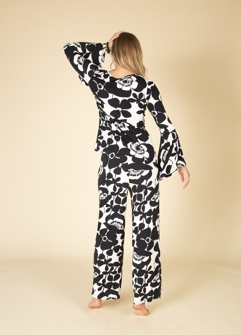 May include: A two-piece outfit featuring a black and white floral pattern. The top has long, flared sleeves and a wrap-style design. The matching pants are wide-legged. The outfit is made of a lightweight fabric.