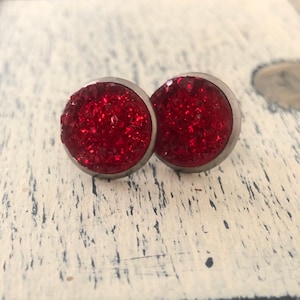 May include: A pair of red glitter stud earrings with silver settings.