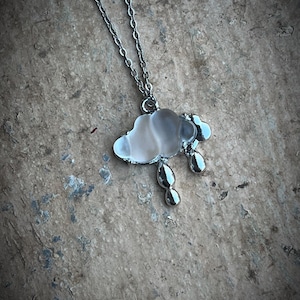 Może przedstawiać: Srebrny łańcuszek z wisiorem w kształcie chmury z przezroczystego szkła i trzema srebrnymi kroplami deszczu zwisającymi z dołu.