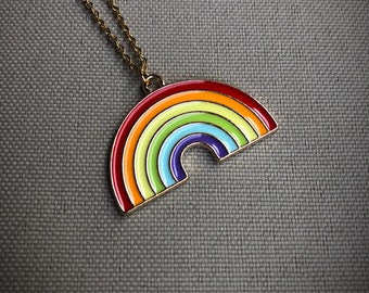 May include: A gold chain necklace with a rainbow-colored enamel pendant in the shape of a rainbow arch.
