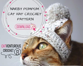 May include: A brown tabby cat wearing a white crocheted hat with a white pompom on top. The hat has a speckled pattern. The cat is looking to the left. The text "NARBY POMPOM CAT HAT CROCHET PATTERN" is in a circle with pink hearts around it. The text "DOWNLOAD" is in a pink button with a white arrow pointing to the right. The text "CATVENTUROUS CROCHET" is below the cat's head with a cat icon. The text "#fashionablycatventurous" is in the bottom right corner.