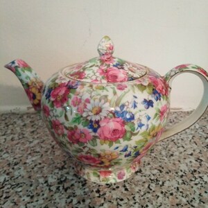 May include: A floral patterned teapot with a lid. The teapot is white with pink, red, yellow, blue, and green flowers.