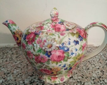 Pode incluir: Uma chaleira com padrão floral e tampa. A chaleira é branca com flores rosa, vermelhas, amarelas, azuis e verdes.