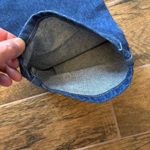 Puede incluir: Primer plano del dobladillo de unos vaqueros azules. El interior del dobladillo es visible, mostrando la textura y las costuras de la tela. Los vaqueros son de un lavado medio y el dobladillo est&aacute; vuelto.