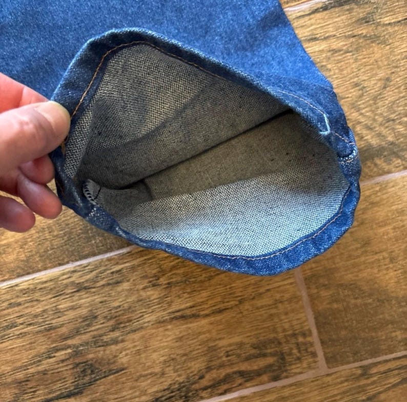 Puede incluir: Primer plano del dobladillo de unos vaqueros azules. El interior del dobladillo es visible, mostrando la textura y las costuras de la tela. Los vaqueros son de un lavado medio y el dobladillo est&aacute; vuelto.
