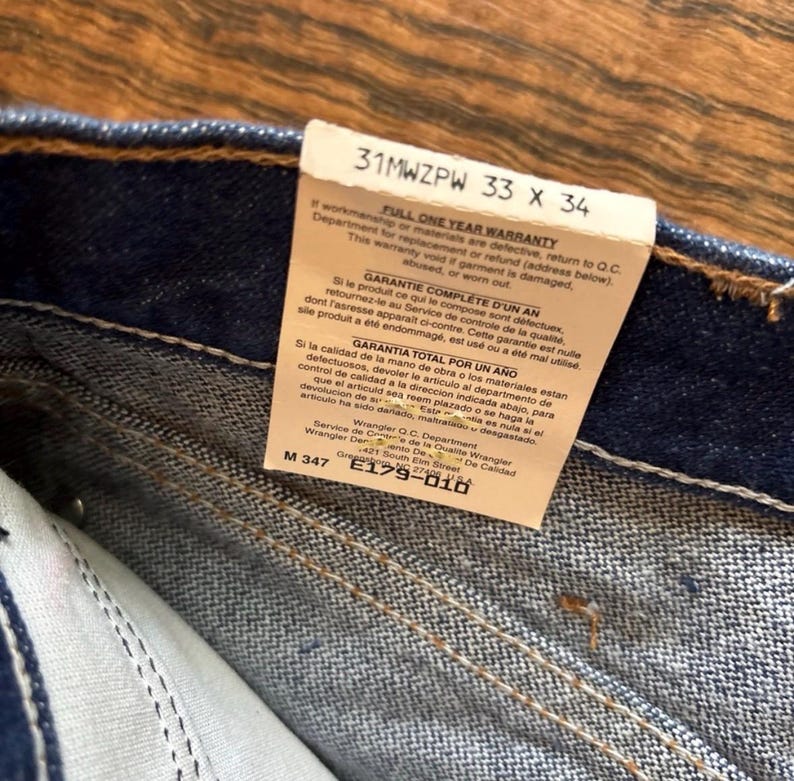 Puede incluir: Primer plano de unos vaqueros azules con una etiqueta blanca adjunta. La etiqueta muestra la talla, "33 X 34", y la informaci&oacute;n de la garant&iacute;a en ingl&eacute;s, franc&eacute;s y espa&ntilde;ol. Los vaqueros son nuevos y muestran los detalles de las costuras.