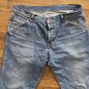 May include: Light blue denim jeans with a button closure and classic five-pocket design. The jeans have a faded wash and copper-colored rivets. The jeans are a classic style.