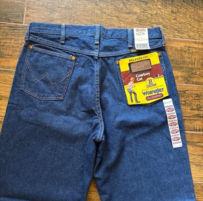 Puede incluir: Vaqueros Wrangler de mezclilla azul oscuro con un corte relajado. Los vaqueros presentan un dise&ntilde;o cl&aacute;sico de cinco bolsillos, un bolsillo trasero con una costura "W" distintiva y una etiqueta "Cowboy Cut". Cintura 79 cm.