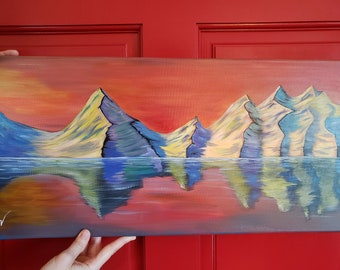 May include: A painting of a mountain range reflected in a still body of water. The mountains are painted in shades of blue, purple, and yellow, with a red and orange sunset sky in the background.
