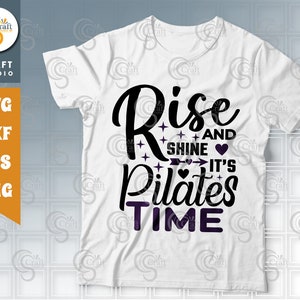 May include: White t-shirt with black text that reads "Rise and Shine It's Pilates Time". The text is decorated with hearts and stars.
