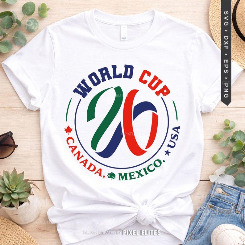 May include: White t-shirt featuring a circular graphic with the text "WORLD CUP 26" in blue, green, and red. The design includes the text "CANADA, MEXICO, USA" and a maple leaf and a star. The shirt is made of a soft material.