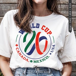 May include: White t-shirt with a colorful graphic design for the 2026 World Cup. The design includes the text "WORLD CUP 26" in blue, green, and red, with "CANADA, MEXICO, USA" in a circular arrangement.