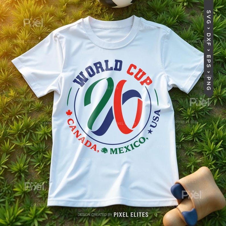 May include: White t-shirt with a circular graphic for the 2026 World Cup. The design includes the text "WORLD CUP 26" and the names of the host countries: Canada, USA, and Mexico. The shirt is on a grassy surface.