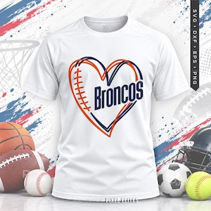 Puede incluir: Una camiseta blanca de manga corta con un gráfico en forma de corazón que recuerda a un balón de fútbol americano con cordones naranjas y la palabra Broncos en letras azul oscuro. El diseño está centrado en el pecho de la camiseta sobre un fondo.