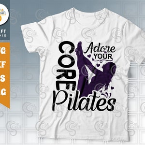 May include: White t-shirt with black text that reads "Core Pilates" and "Adore Your" with a silhouette of a person doing a pilates pose.
