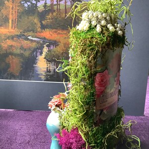 May include: A glass bottle decorated with moss, pearls, and a floral design. The bottle has a label that reads "Eau de Rose, Pure Petals".