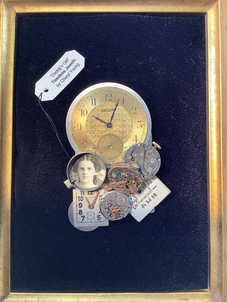 May include: A framed mixed media artwork featuring a vintage clock face, watch parts, and a small photograph of a young girl. The artwork is titled "Daddy's Girl Timeless Jewels by Cheryl Young".