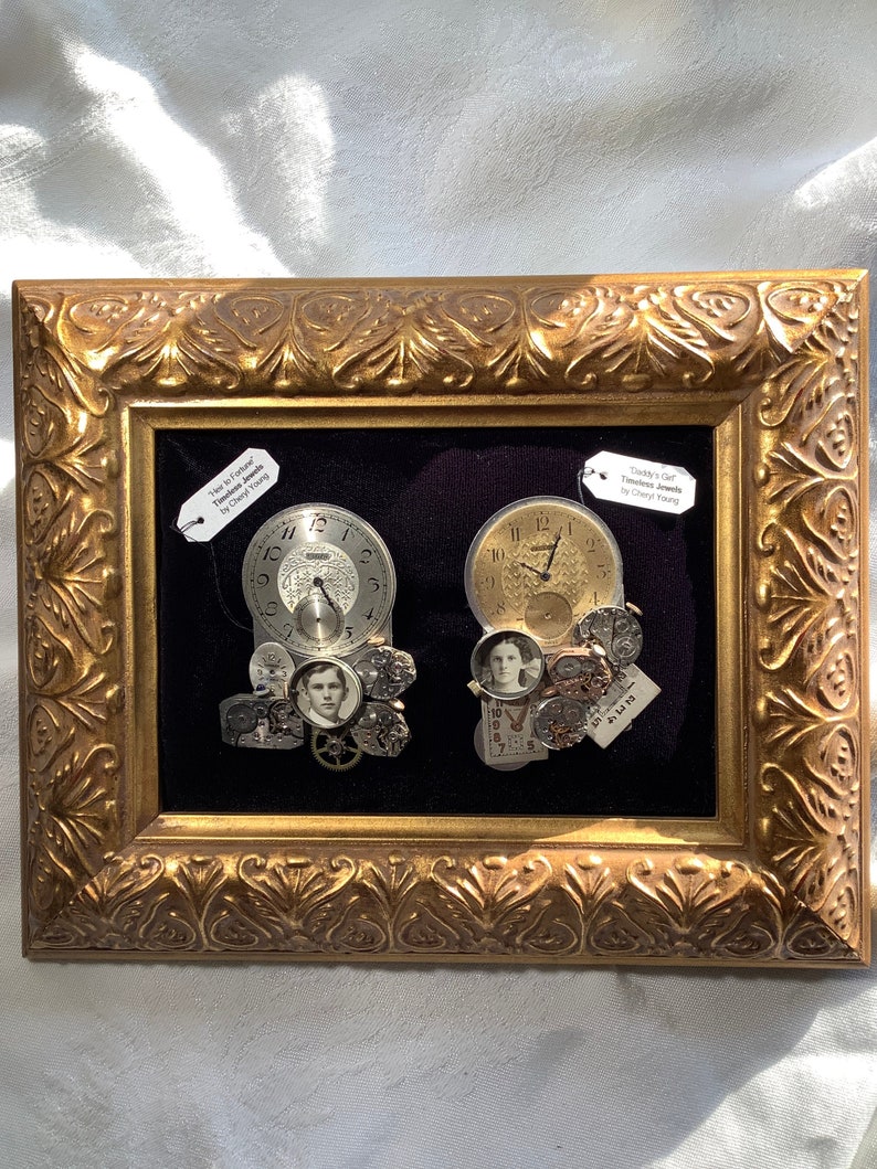 May include: Two framed pieces of art featuring vintage pocket watches and other clock parts, with a black background. The top label on the left reads "Hero to Captain" Timeless Jewels by Cheryl Young. The top label on the right reads "Daddy's Girl" Timeless Jewels by Cheryl Young.
