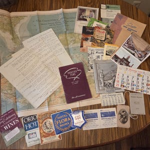 May include: A collection of vintage ephemera, including maps, recipe books, and a calendar. The items are arranged on a wooden surface. Notable items include a map of the Caribbean, a calendar from January 1950, and various labels and brochures.