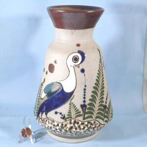 May include: A white ceramic vase with a brown rim and a painted design of a blue and white bird with green foliage.