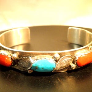 May include: A silver bracelet with turquoise and coral stones. The bracelet has a simple design with a band of silver and a row of stones.
