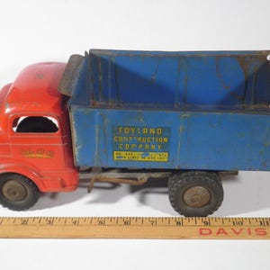 May include: Vintage red and blue Toyland Construction Company dump truck. The truck features a red cab and a blue dump bed with the company's name and details. The truck has black tires and a metal construction.