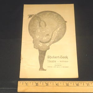 May include: A black and white image of a woman playing a lute. The image is on a programme for the Shubert-Geek Theatre in Buffalo, New York.