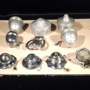 May include: Collection of vintage tea infusers in various shapes and designs. Includes spherical, acorn, and teapot-shaped infusers, all made of silver-toned metal. Some have chains and small saucers. A charming assortment for tea lovers.