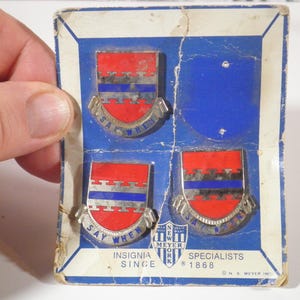 May include: Vintage pin set featuring four shield-shaped insignia with red, silver, and blue designs. Each pin has the words "SAY WHEN" and is set on a blue and white cardboard backing. The text "INSIGNIA SINCE 1868" is also visible.