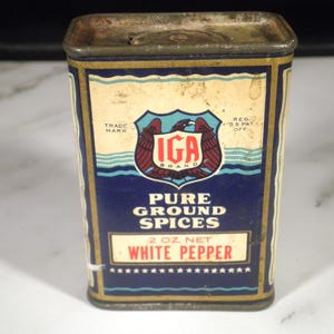 May include: Vintage IGA Grand Pure Ground Spices tin, featuring a blue and cream label with the text "White Pepper" and a 2 oz net weight. The label includes the IGA brand logo and the words "Trade Mark" and "Reg. U.S. Pat. Off."