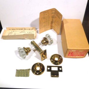 May include: A vintage Hampton door latch set with clear glass knobs and brass hardware. The set includes a box, diagrams, and various components. The box has the words "Hampton" and "Latch Set" printed on it.