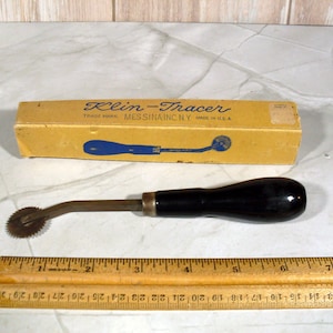 May include: A Klin-Tracer sewing tool with a black wooden handle and a metal tracing wheel, accompanied by its original yellow cardboard box labeled Messina Inc. N.Y. Made in U.S.A. A wooden ruler is positioned below, showing a length of 8 inches.