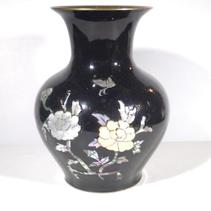 May include: Black vase with a gold rim and floral design. The vase features white and yellow flowers with iridescent accents. The vase has a glossy finish and a classic shape, suitable for home decor.