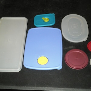 Puede incluir: Surtido de recipientes de almacenamiento de alimentos de plástico con tapas en varios colores, incluidos azul, blanco, rojo y amarillo. Las tapas tienen una variedad de formas y tamaños.