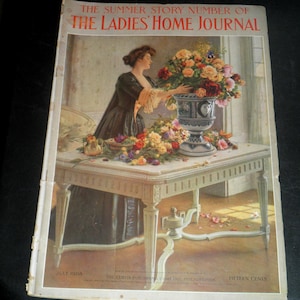 May include: A vintage magazine cover for The Ladies' Home Journal, July 1908. The illustration depicts a woman arranging flowers in a large vase on a white table. The table is ornate, and the scene is set indoors with a window in the background. The magazine title is at the top.