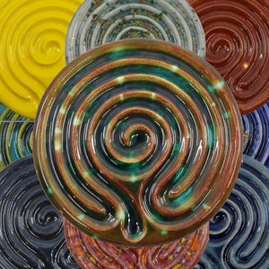 May include: A selection of ceramic labyrinth bowls in various colours, including yellow, green, brown, and blue. Each bowl features a spiral design, with a glossy finish. The bowls are arranged in a circular pattern.