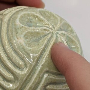 May include: A ceramic sphere with a green glaze and a raised, geometric pattern. The sphere has a smooth, glossy finish.
