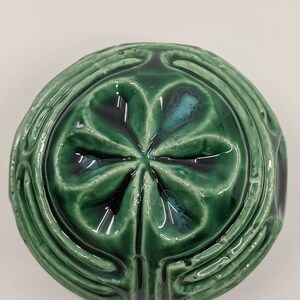 May include: A green ceramic ornament with a four-leaf clover design. The ornament has a glossy finish and intricate details.