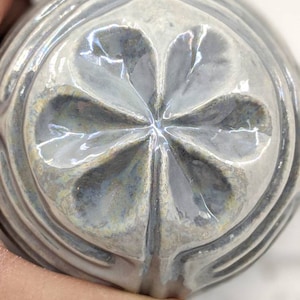 May include: A white ceramic ornament with a four-leaf clover design. The ornament has a glossy finish and a raised design.