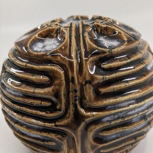 May include: A brown ceramic sphere with a textured surface and white accents. The sphere has a unique, organic design.